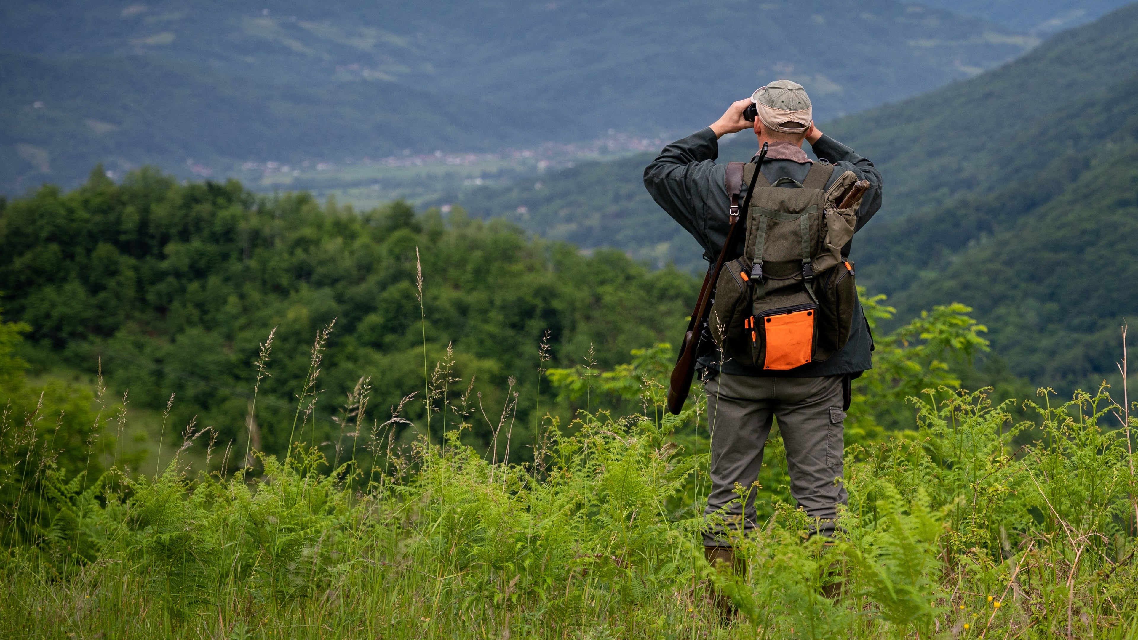 Jäger auf einer grünen Lichtung schaut mit einem Fernglas in ein Tal herunter