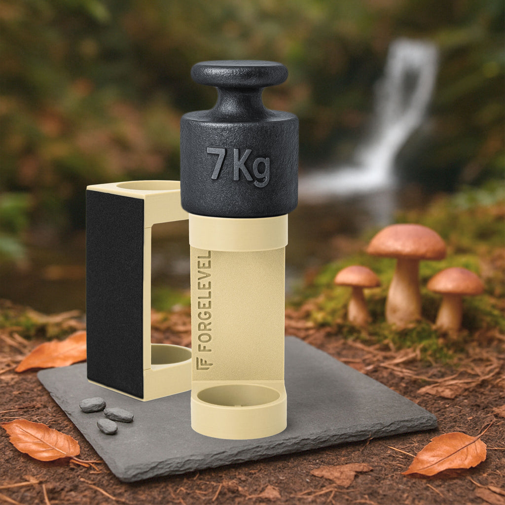 Schwarzes 7-Kilogramm-Gewicht auf beigem Halter mit der Aufschrift FORGELEVEL auf grauer Steinplatte im Wald mit Pilzen und Herbstlaub