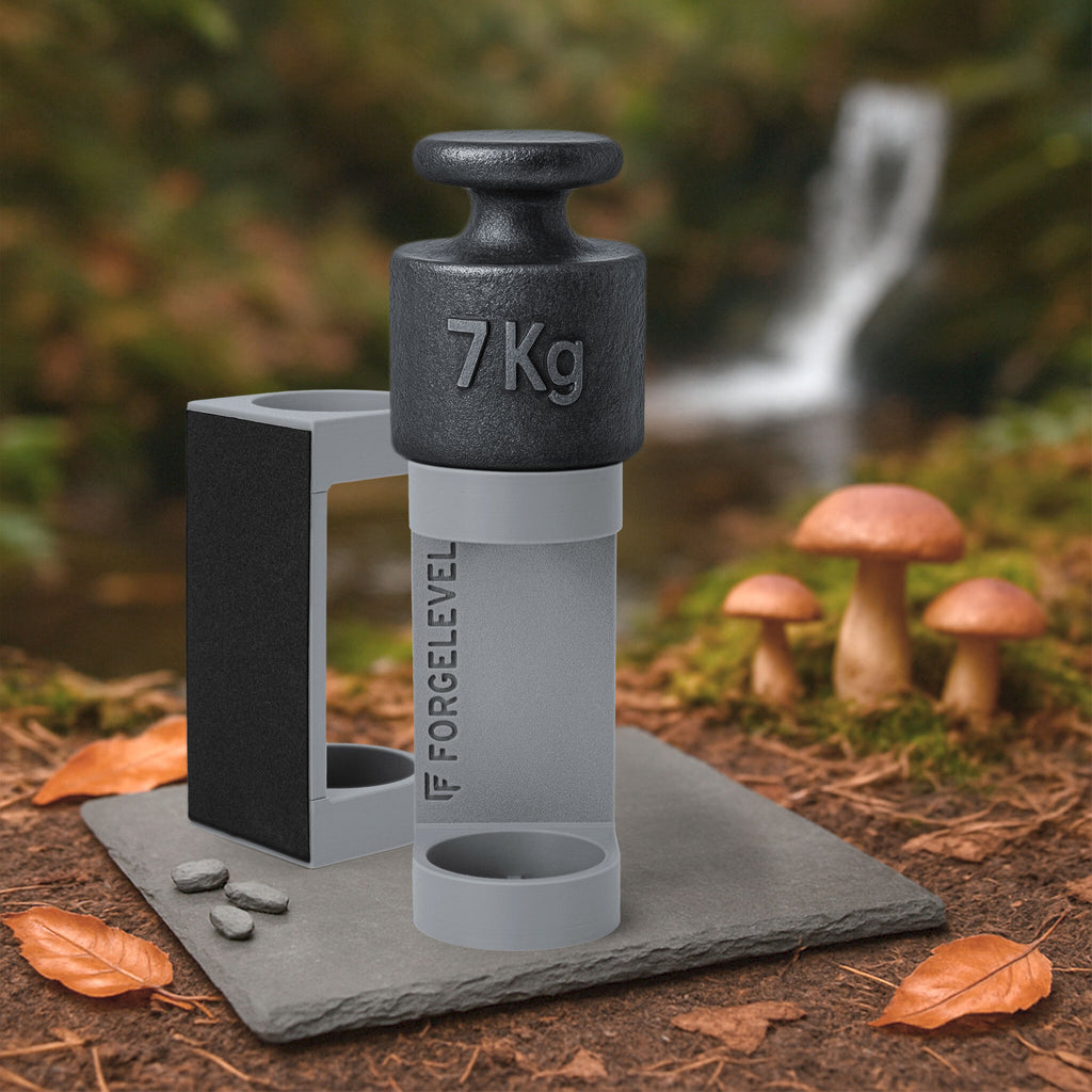 Schwarzes 7-Kilogramm-Gewicht auf grauem Halter mit der Aufschrift FORGELEVEL auf grauer Steinplatte im Wald mit Pilzen und Herbstlaub