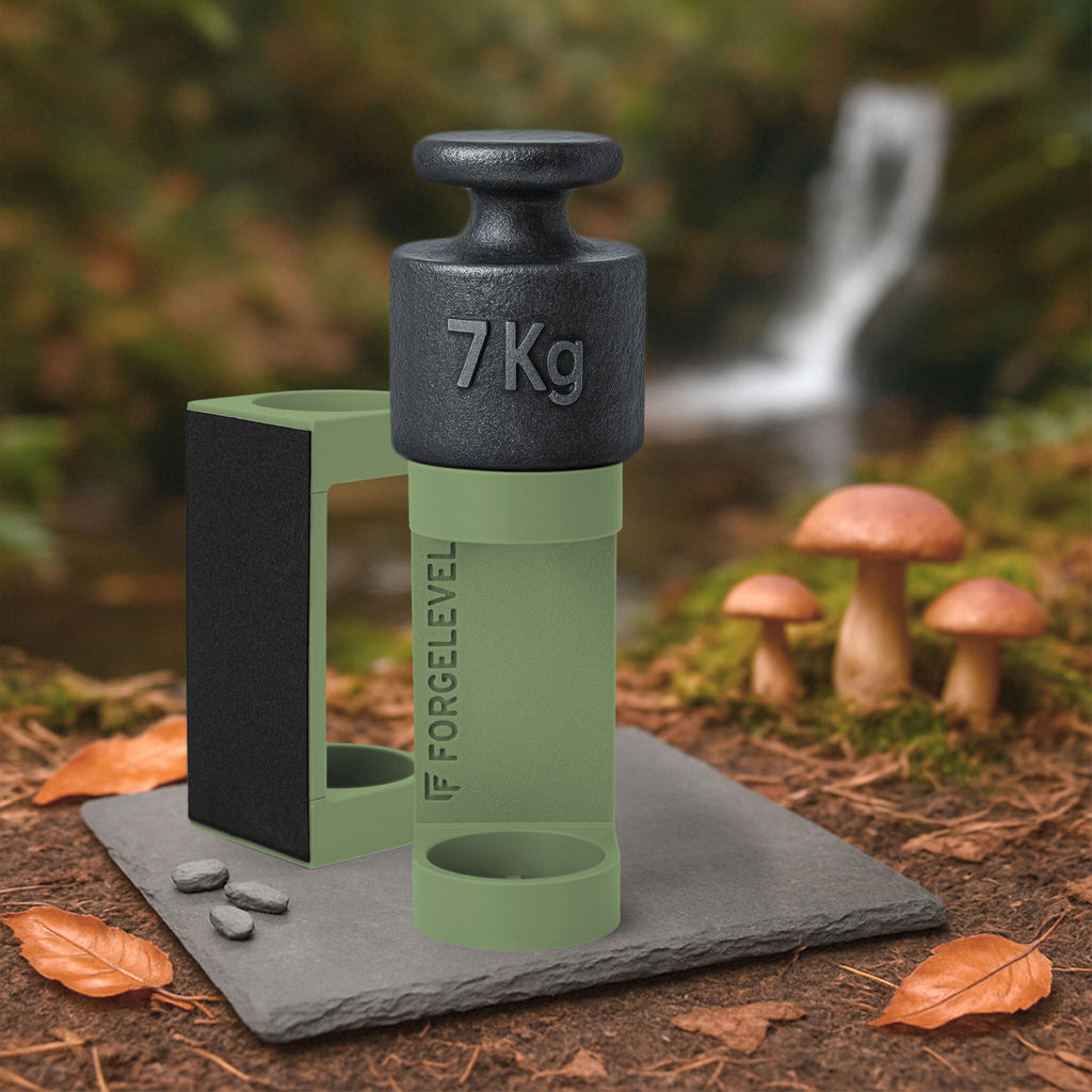 Schwarzes 7-Kilogramm-Gewicht auf olivem Halter mit der Aufschrift FORGELEVEL auf grauer Steinplatte im Wald mit Pilzen und Herbstlaub