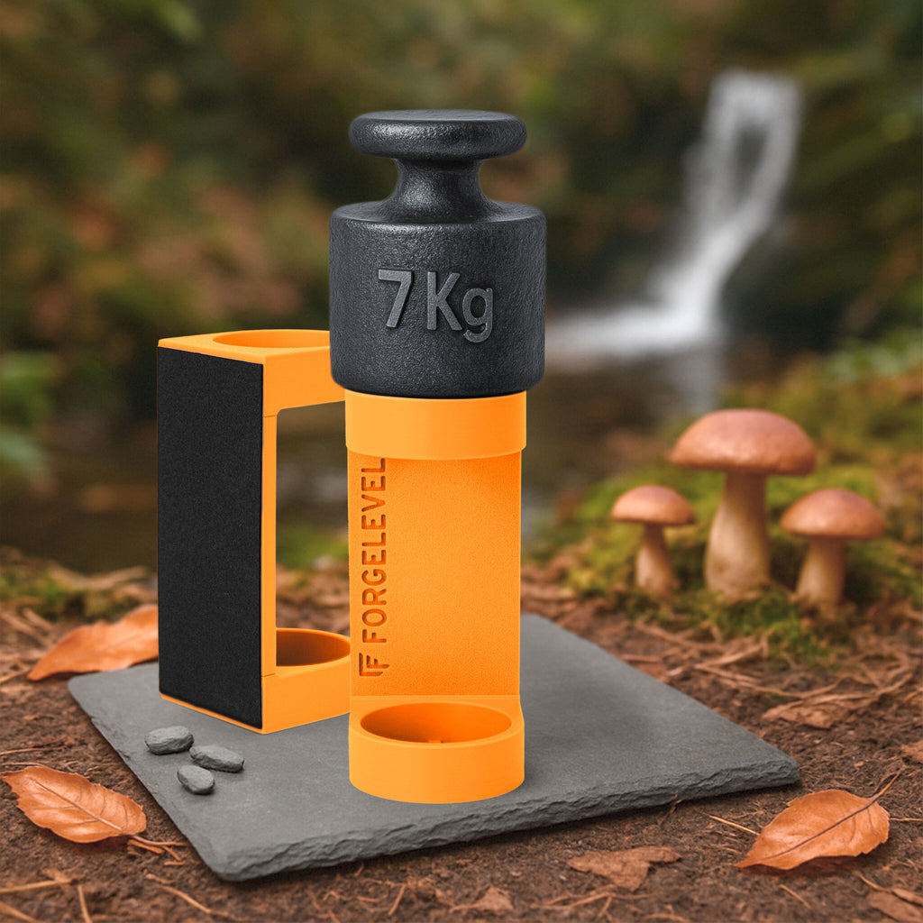 Schwarzes 7-Kilogramm-Gewicht auf orangenem Halter mit der Aufschrift FORGELEVEL auf grauer Steinplatte im Wald mit Pilzen und Herbstlaub