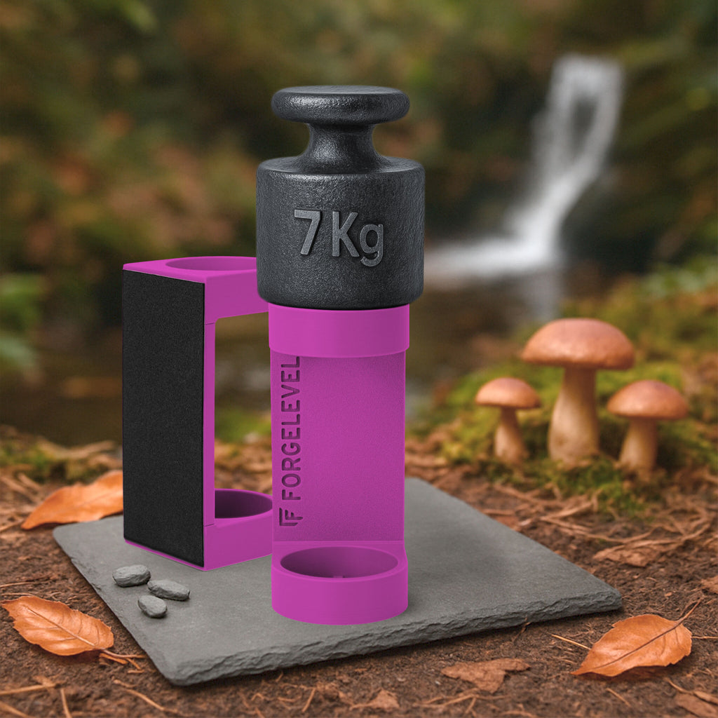 Schwarzes 7-Kilogramm-Gewicht auf pinkfarbenem Halter mit der Aufschrift FORGELEVEL auf grauer Steinplatte im Wald mit Pilzen und Herbstlaub